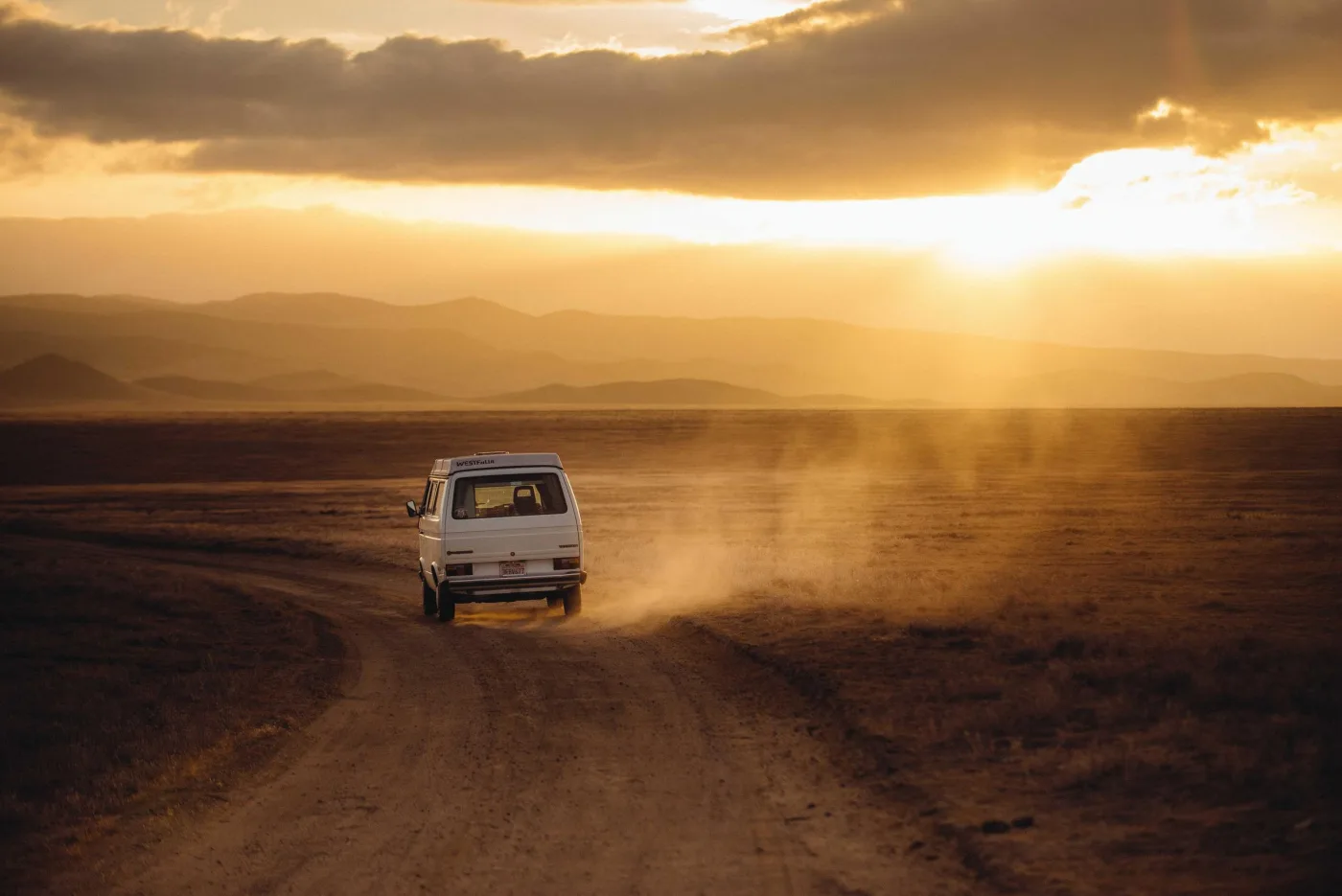 Carro em estrada de terra levantando poeira ao pôr do sol