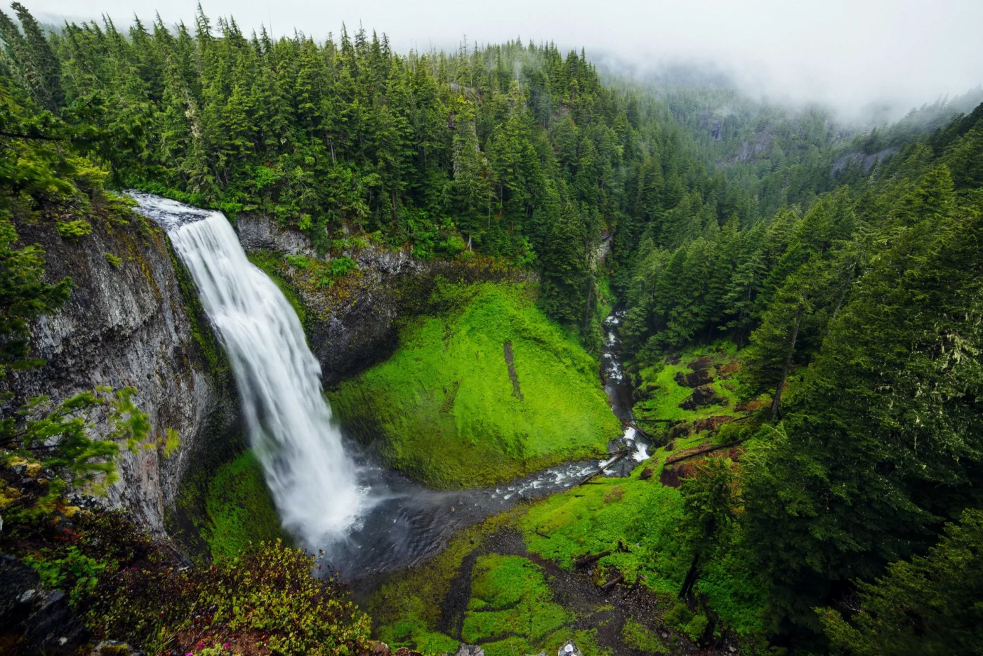 Cachoeira caindo em vale verde cercado de montanhas