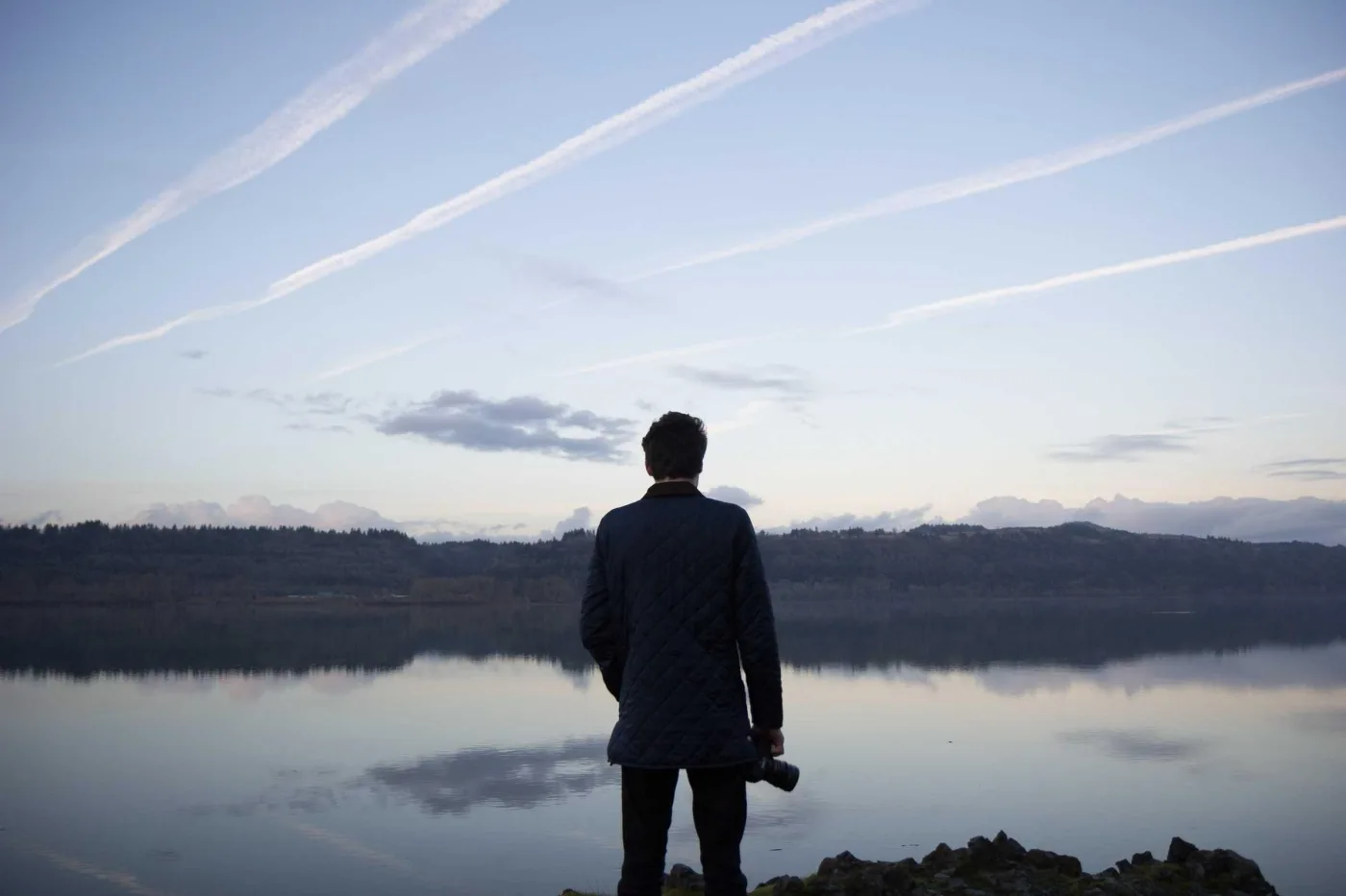 Homem de costas diante de lago ao entardecer
